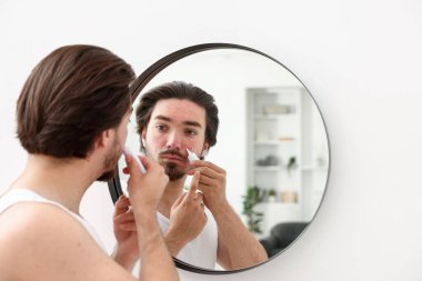 Evinde aynanın yanında yüzüne krem sürmekte zorlanan genç bir adam.