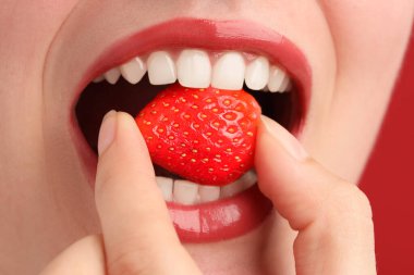 Güzel dudakları olan ve kırmızı arka planda çilekli bir kadın, yakın plan.