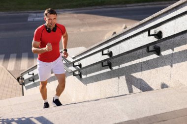 Spor kıyafetli bir adam merdivenlerden dışarı koşuyor.