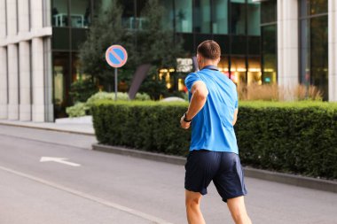 Spor giyimli bir adam dışarıda koşuyor.