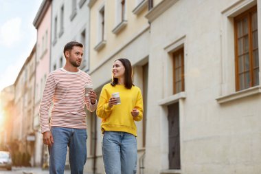 Paket kahve. Kağıt bardakta içki içen çift şehir caddesinde yürüyor, düşük açılı. Metin için boşluk