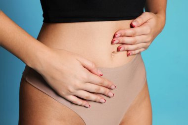 Açık mavi arka planda düz göbekli genç kadın, yakın plan.