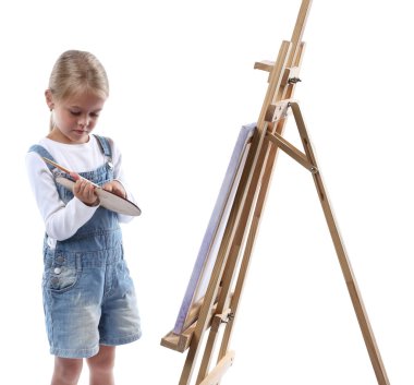 Meslek seçimi. Beyaz arka planda ressammış gibi davranan palet boyalı ve sehpanın yanındaki fırçalı küçük kız.