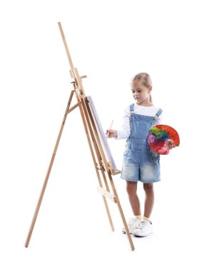 Meslek seçimi. Beyaz arka planda ressammış gibi davranan palet boyalı ve sehpanın yanındaki fırçalı küçük kız.