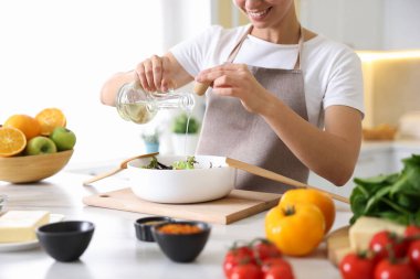 Yemek pişirme süreci. Gülümseyen kadın salataya yağ döküyor.