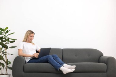Evdeki kanepede dizüstü bilgisayarı olan kadın. Metin için boşluk