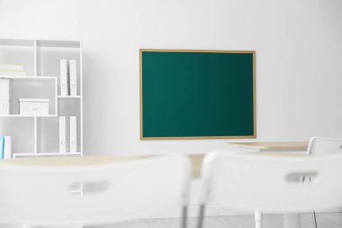 Boş yeşil karatahta, masalar, sandalyeler ve raf ünitesi sınıfta.