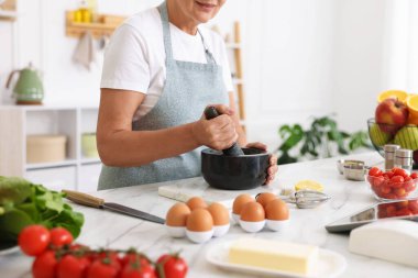 Üst düzey kadın mutfaktaki beyaz mermer masada yemek pişiriyor.