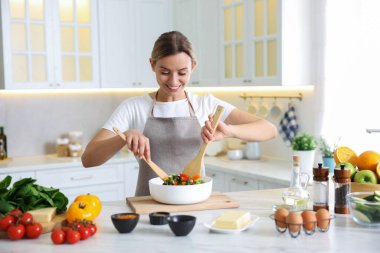 Mutfaktaki masada yemek yapan gülümseyen kadın.