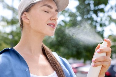 Beyzbol şapkalı güzel bir kadın yüzüne termal su püskürtüyor.