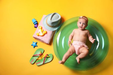 Sarı arka planda şişme yüzük ve plaj aksesuarları olan şirin bir bebek.