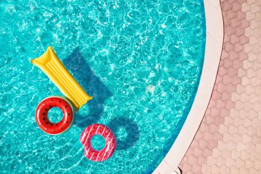 Yüzme havuzunda yüzen şişme halkalar ve şilte, üst manzara. Yaz tatili