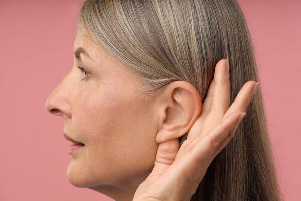 Звук. Старшая женщина показывает руку к уху жест на розовом фоне