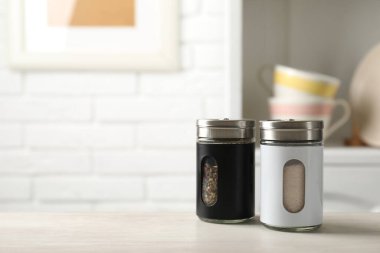 Salt and pepper shakers on light wooden table in kitchen, closeup. Space for text