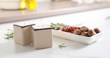 Salt, pepper shakers and spices on white marble table indoors, closeup