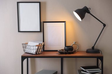 Stylish lamp, other decor and books on console table near beige wall indoors
