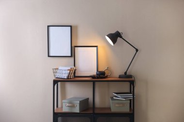 Stylish lamp, other decor and books on console table near beige wall indoors