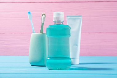Mouthwash, toothpaste and toothbrushes on blue wooden table against pink background. Oral hygiene