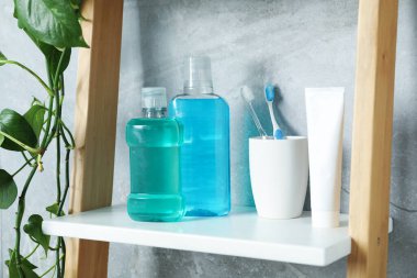 Bottles of mouthwash, toothbrushes and toothpaste on shelf in bathroom