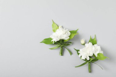 Boutonnieres with beautiful flowers on light background, flat lay. Space for text