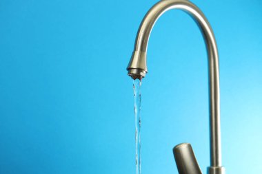 Su tasarrufu konsepti. Açık mavi arkaplandaki musluktan akan su akıntısı, yakın plan. Metin için boşluk