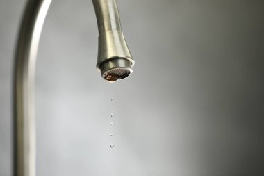 Su tasarrufu konsepti. Gri arka planda musluktan su damlıyor, yakın plan. Metin için boşluk