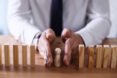 Risk. Adam masadaki tahta figürü korumak için domino efektini durduruyor.