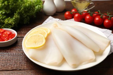 Pieces of raw squids with lemon on wooden table, closeup