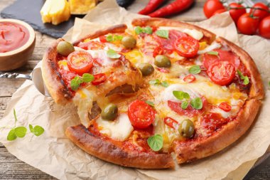 Taking piece of delicious pizza with cheese, tomatoes and olives at wooden table, closeup