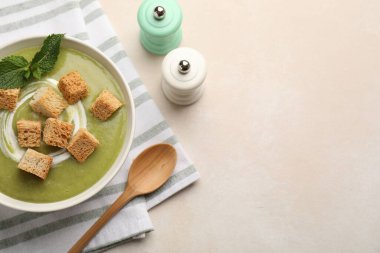 Salt and pepper mills near bowl of delicious cream soup with croutons and mint on light table, flat lay. Space for text
