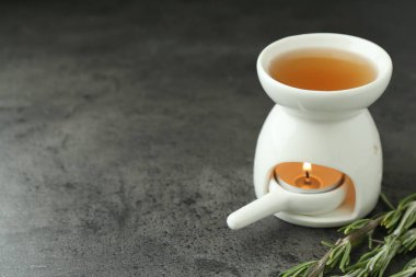 Aroma lambası, yanan mum ve gri desenli masada biberiye, yakın plan. Metin için boşluk