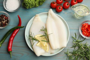 Limon dilimli pişmemiş mürekkep balıkları, biberiye ve baharatlar mavi ahşap masada, düz yatıyordu.