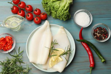 Limon dilimli pişmemiş mürekkep balıkları, biberiye ve baharatlar mavi ahşap masada, düz yatıyordu.