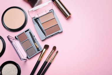 Renkli göz falı paletleri, pudraları ve pembe arka planda makyaj fırçaları olan düz bir kompozisyon. Metin için boşluk