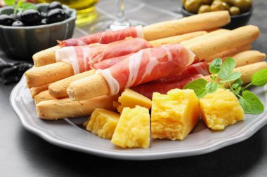 Grissini ekmek çubukları, jambon ve peynirli gri masada, yakın plan.