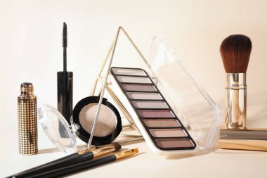 Stylish presentation of colorful eyeshadow palette, mascara and makeup brushes on beige background, closeup