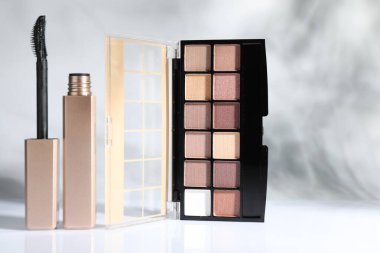 Eyeshadow palette and mascara on mirror surface against white background