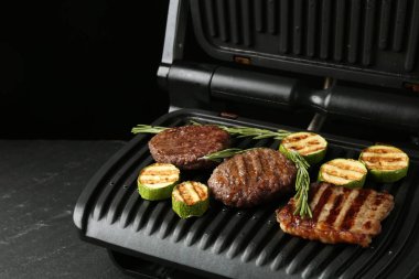 Biftekli elektrikli ızgara, kabak ve biberiye siyah masada, yakın plan. Metin için boşluk