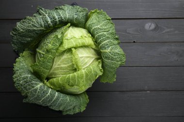 Fresh Savoy cabbage on black wooden table, top view. Space for text