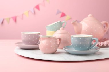 Ahşap masadaki çocuklar için güzel seramik çay seti. Pembe arka planda, parti bayraklarıyla, yakın plan.