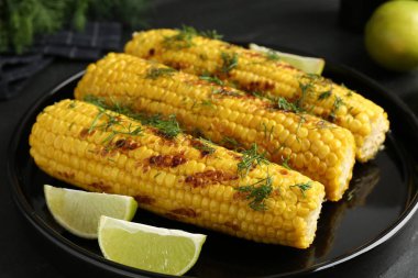 Lezzetli ızgara mısır koçanlarıyla siyah masada dereotu ve limon dilimleri, yakın plan.