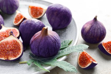 Taze incir ve yeşil yaprak gri masada, yakın plan.