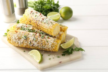 Beyaz ahşap masada maydanozlu, peynirli ve limonlu mısır koçanları.