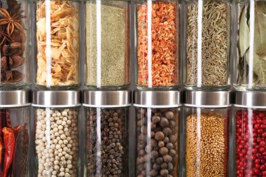 Cam kavanozlardaki farklı baharatlar gri arka planda, yakın plan