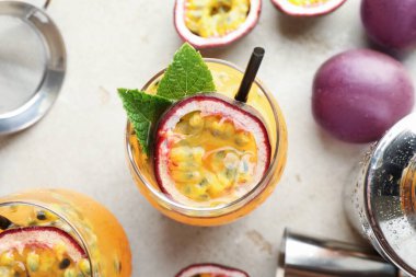 Lezzetli tutkulu meyve suyu bardakta nane, taze meyve ve barmenin aletleri gri masada, düz yerde.