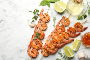 Skewers with tasty grilled shrimps, lime slices, herbs, oil and sauce on white marble table, flat lay with space for text. Delicious seafood dish