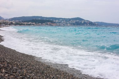 Dalgalı deniz manzarası ve kumsaldaki çakıl taşları.