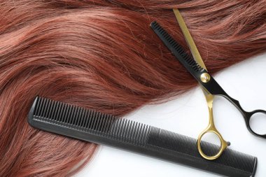 Beyaz arka planda kestane rengi saç teli ve kuaför aletleri var.