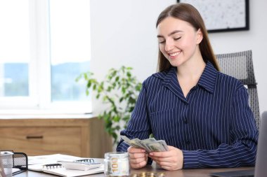 Kadın içeride ahşap masada dolar sayıyor, mesaj için yer var.