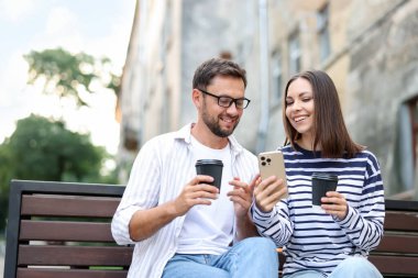 Paket kahve. Açık hava bankında kağıt bardaklar ve akıllı telefonlar olan bir çift.